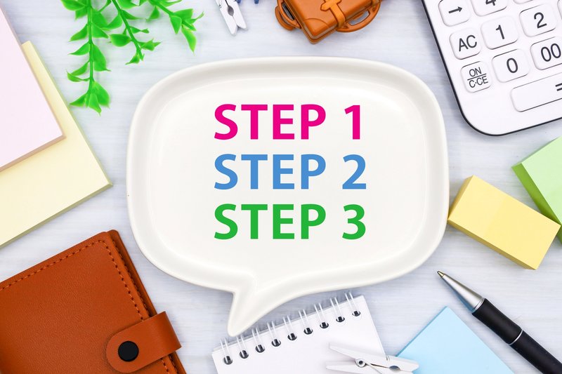 STEP1・STEP2・STEP3と書かれた吹き出しプレートと電卓・手帳などのビジネス文具